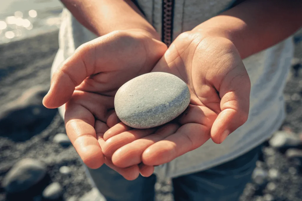 A pair of hands gently holding a simple stone, an example of finding the sacred in the ordinary on a journey of spiritual growth.